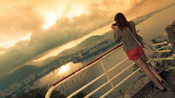 Female tourist taking a picture of the sunset from a look-out point in Rio, Brazil